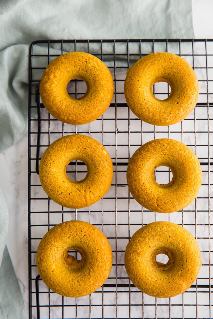 baked pumpkin vegan donuts laying on a wire rack on top of a green kitchen towel