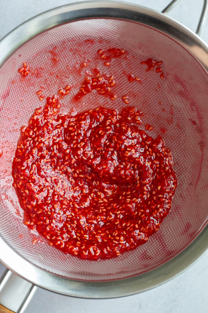 Straining out seeds from cooked raspberries in a sieve. 