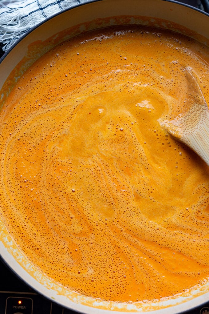 Stirring red pepper pasta sauce in a large pot.