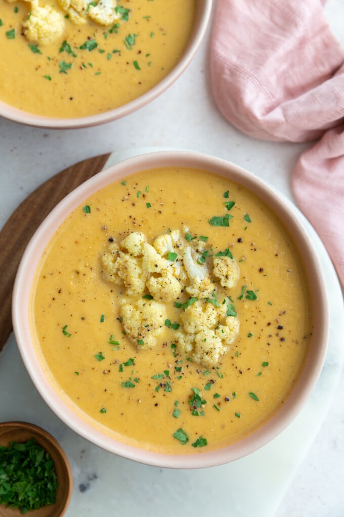 big pink bowl filled with orange cauliflower soup topped with roasted cauliflower and fresh herbs