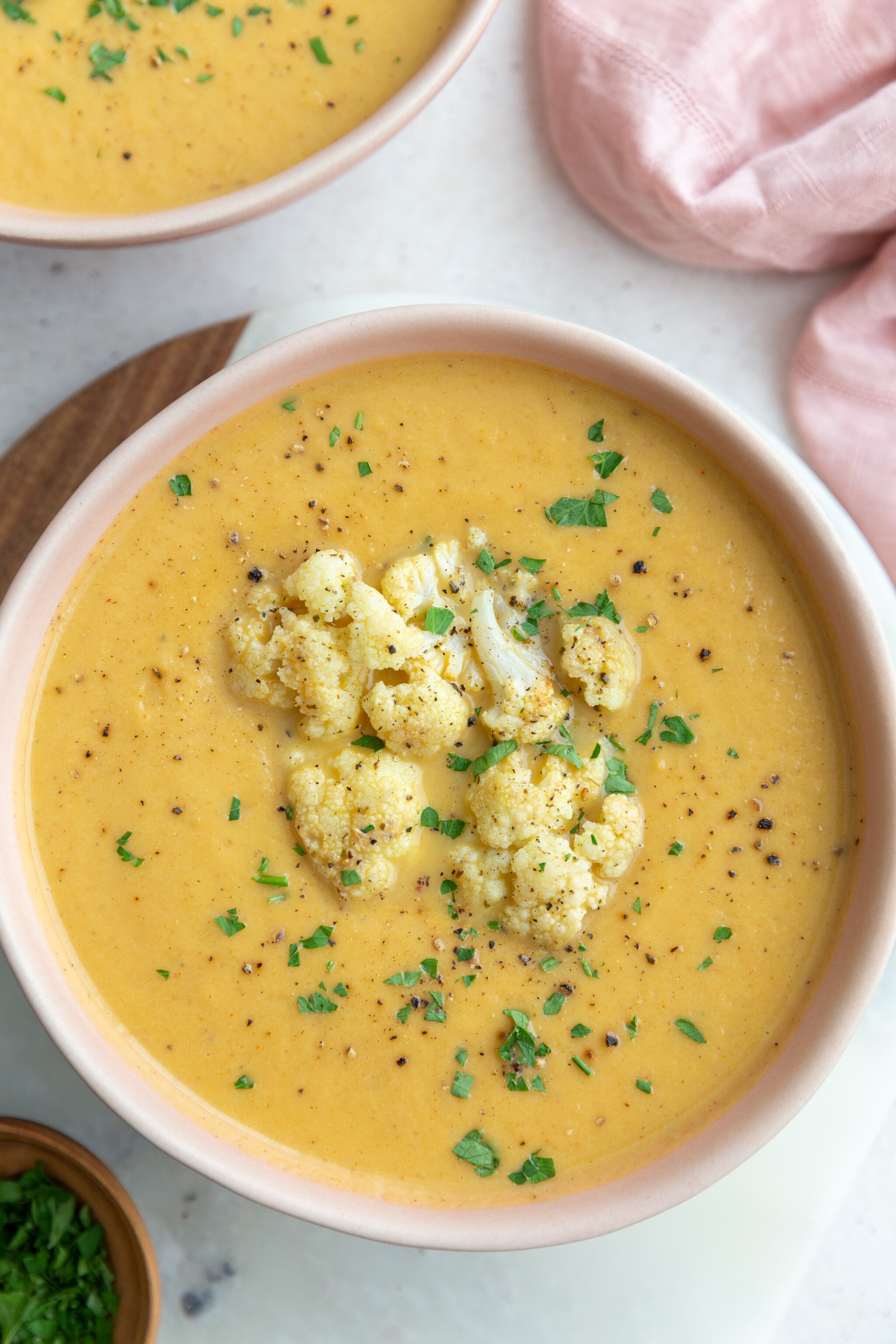 big pink bowl filled with orange cauliflower soup topped with roasted cauliflower and fresh herbs