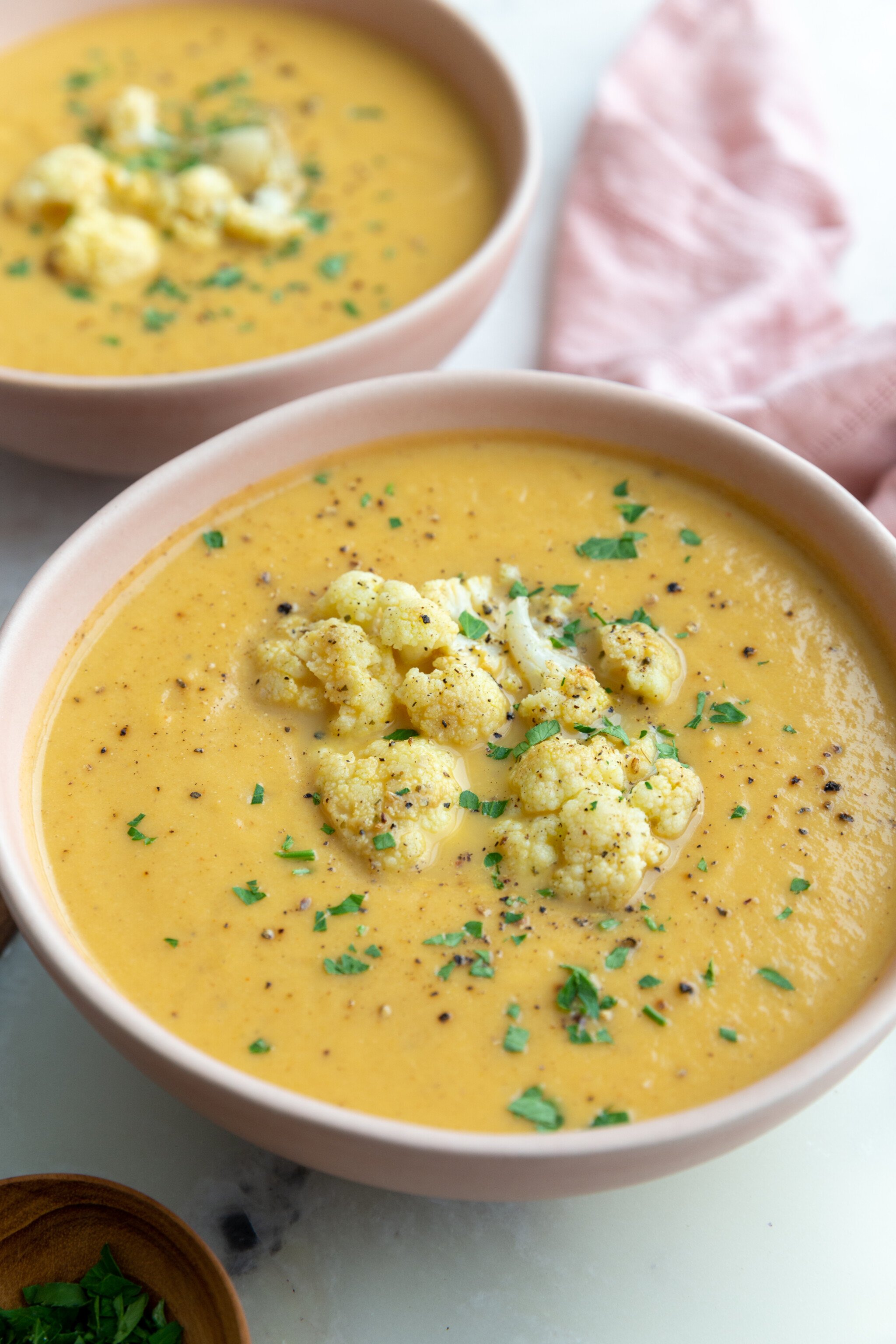 big pink bowl filled with orange cauliflower soup topped with roasted cauliflower and fresh herbs