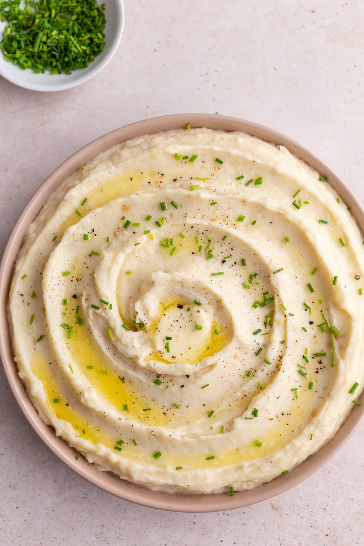 mashed potatoes swirled into a pink dish and topped with chives. bowl of chives in the corner