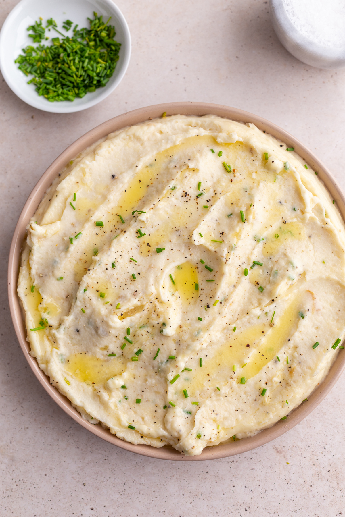 mashed potatoes swirled into a pink dish and topped with chives. bowl of chives in the corner