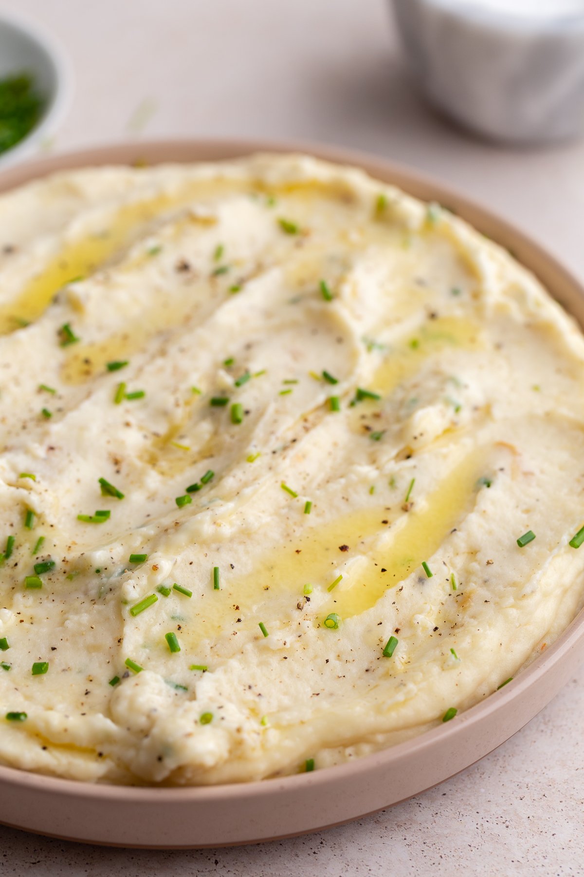 mashed potatoes swirled into a pink dish and topped with chives. bowl of chives in the corner