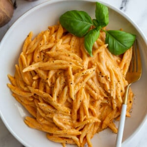 Spiral pasta in a roasted red pepper sauce in a large wide bowl with basil on top