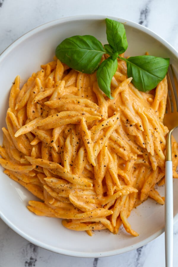 Spiral pasta in a roasted red pepper sauce in a large wide bowl with basil on top