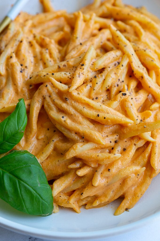 up close shot of Spiral pasta in a roasted red pepper sauce in a large wide bowl with basil on top