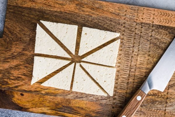 overhead shot of tofu cut into triangles. sitting on a wood cutting board with a knife in the corner