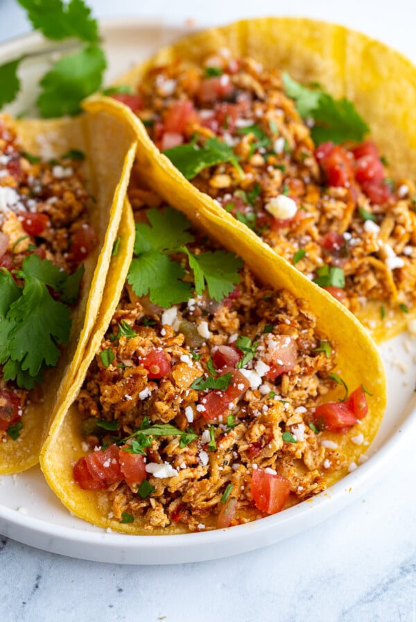 shredded tofu tacos made with corn tortillas and topped with cotija cheese, chopped cilantro, and diced tomatoes