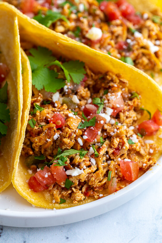 shredded tofu tacos made with corn tortillas and topped with cotija cheese, chopped cilantro, and diced tomatoes