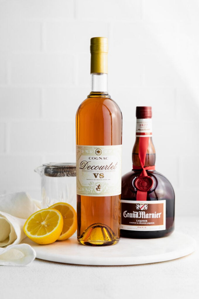 ingredients laid to out make a sidecar drink including lemon juice, cognac, and orange liqueuer