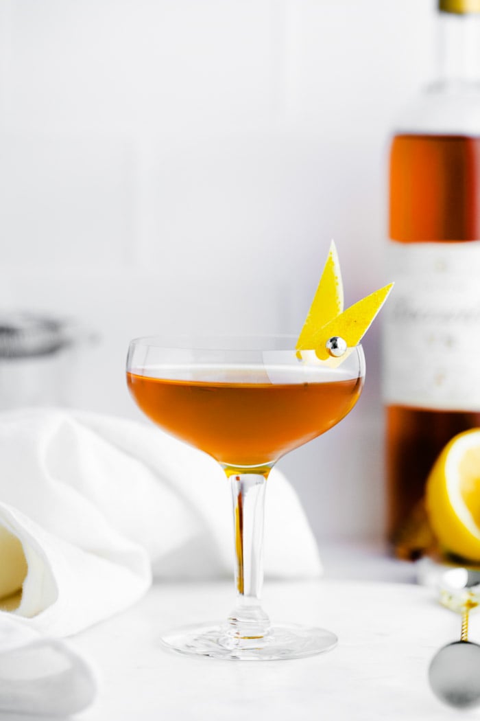 sidecar cocktail in a coupe glass with lemon peel on the side and alcohol bottle on the background