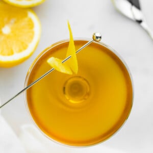 orange looking cocktail in a coupe glass with lemon on the side photographed from the top down