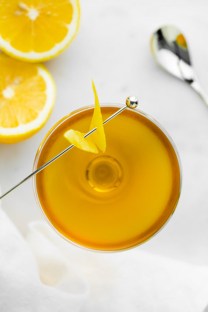 orange looking cocktail in a coupe glass with lemon on the side photographed from the top down