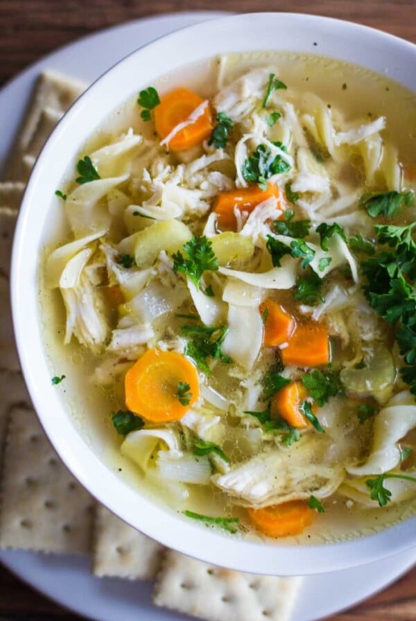 chicken noodle soup in a white bowl with crackers around it