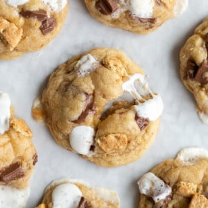 s'mores cookies on a baking tray. One of the cookies is puled apart so you can see the gooyness of he marshmallow on the cookies