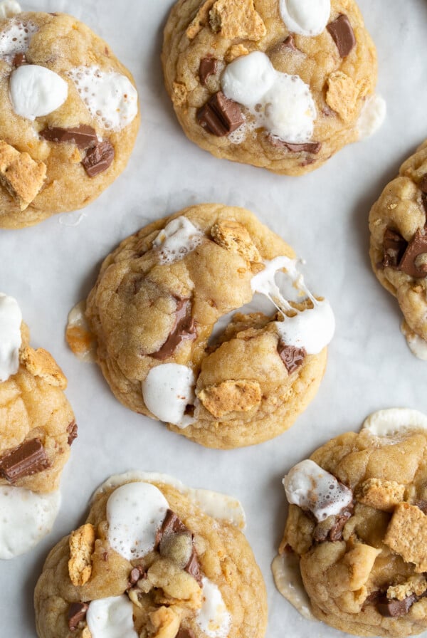 s'mores cookies on a baking tray. One of the cookies is puled apart so you can see the gooyness of he marshmallow on the cookies