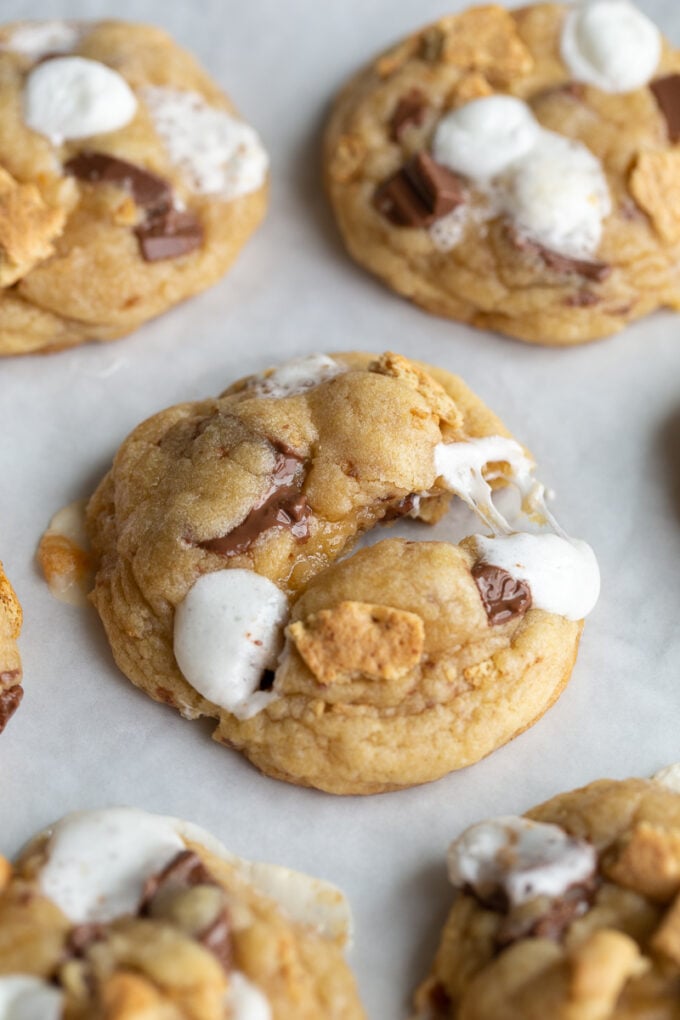 s'mores cookies on a baking tray. One of the cookies is puled apart so you can see the gooyness of he marshmallow on the cookies