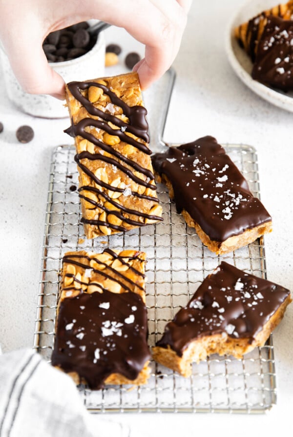 healthy granola bars drizzled with chocolate and sprinkled with sea salt and hand holding one up