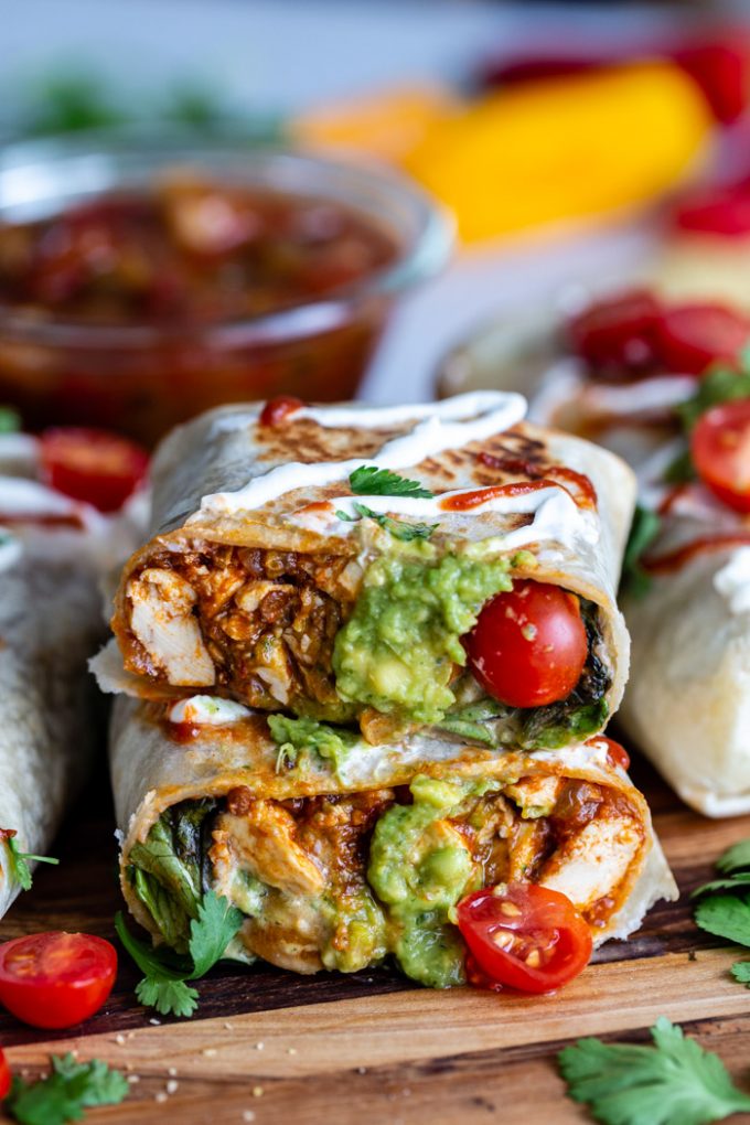 burrito cut in half so you can see the inside filled with spicy tofu, guacamole, lettuce and tomatoes. more burritos in the background