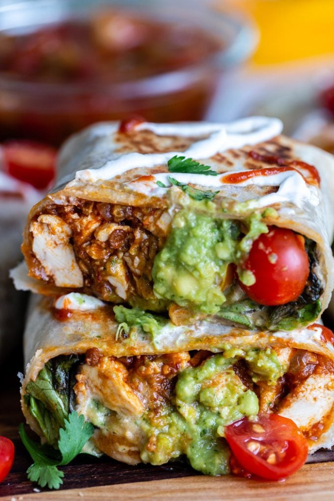 burrito cut in half so you can see the inside filled with spicy tofu, guacamole, lettuce and tomatoes. more burritos in the background