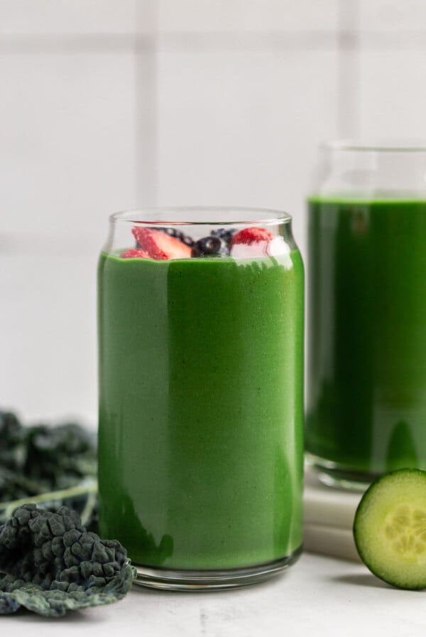 Green smoothie in a large glass topped with berries.