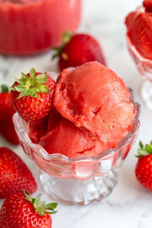 Strawberry sorbet in an ice cream dish with strawberries around the scene