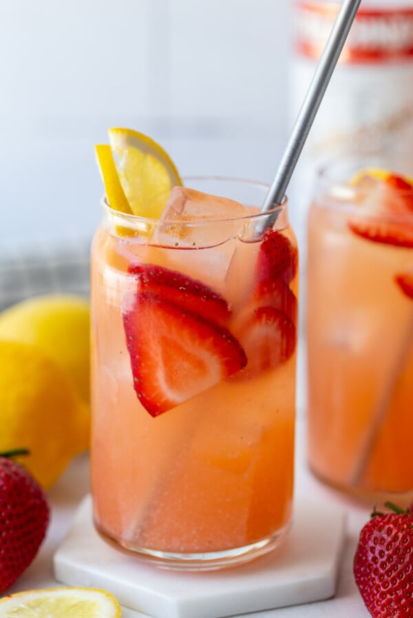 glass filled with strawberry lemonade vodka with a bottle of vodka in the background and garnished with fresh lemon and strawberries