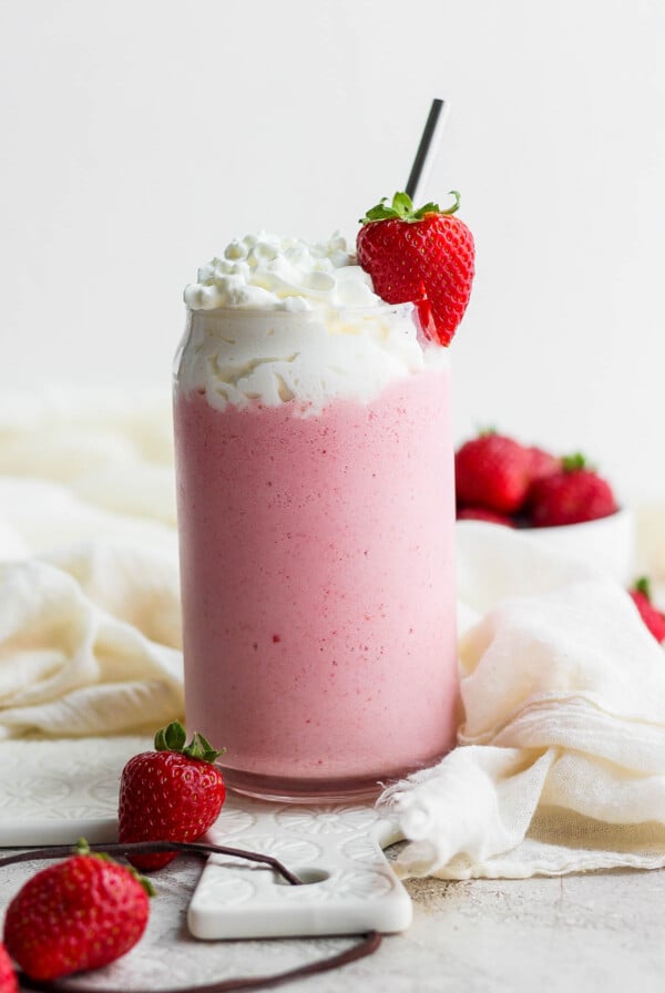 strawberry milkshake with whipped cream and a fresh strawberry on top and a straw in the cup