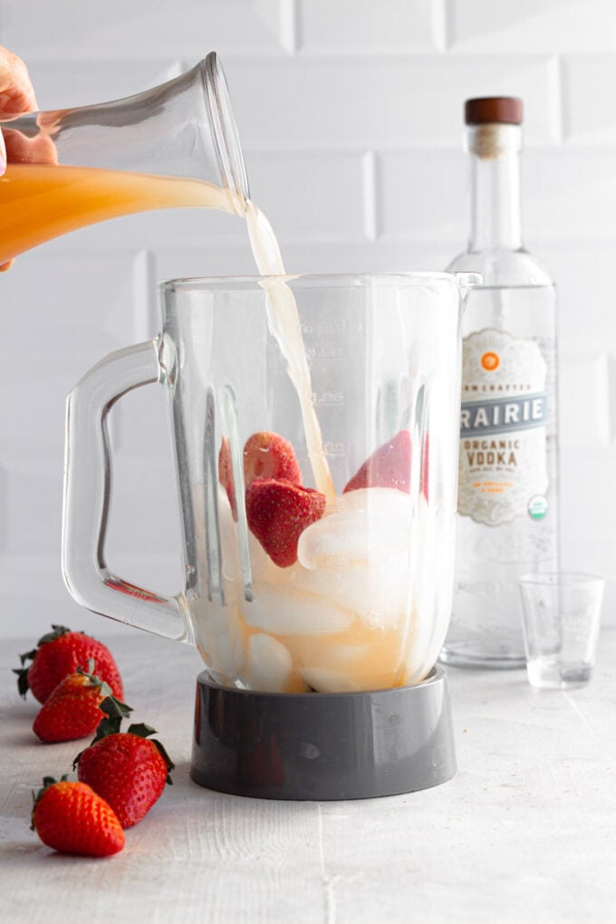 blender full of ice and strawberries with grapefruit juice being poured in