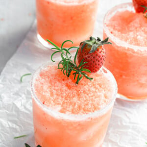 small glass with a frozen salty dog slushie with fresh strawberries and rosemary on top