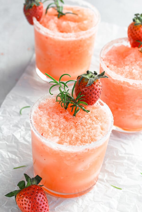 small glass with a frozen salty dog slushie with fresh strawberries and rosemary on top