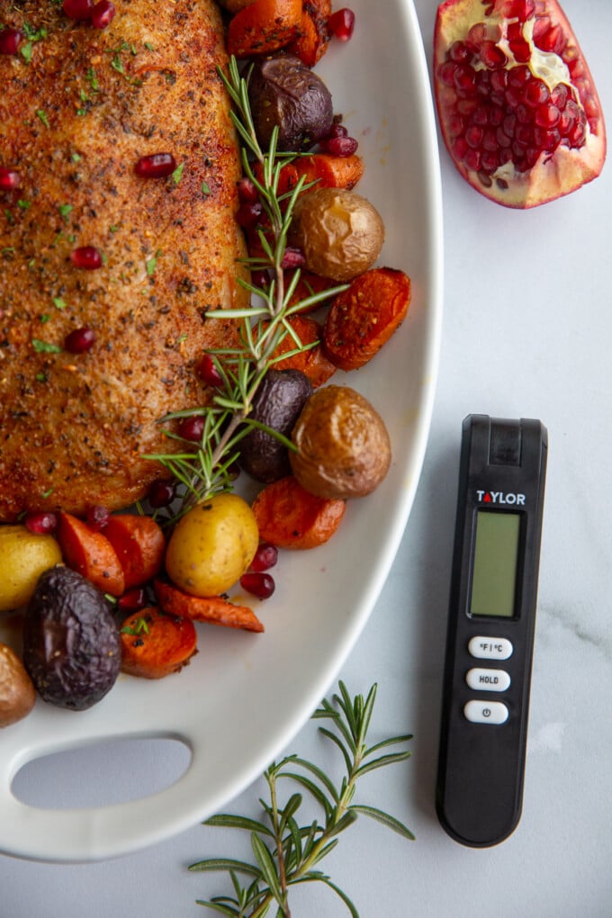 stuffed vegan roast surrounded by roasted veggies on a platter. the photo is off center and on the side is a Taylor kitchen thermometer