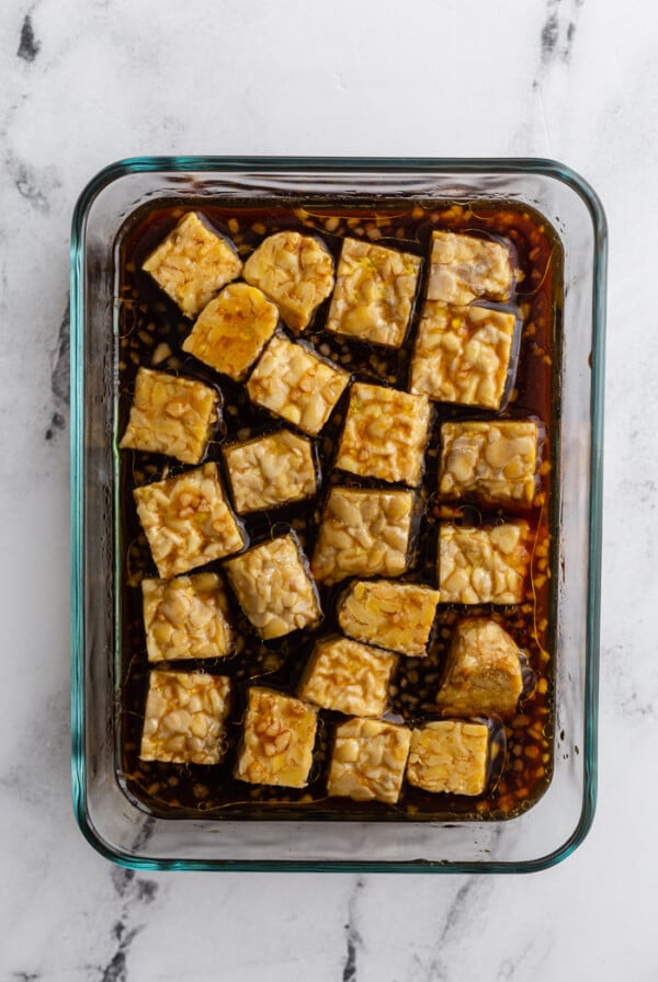 glass container with tempeh marinating in a dark sauce