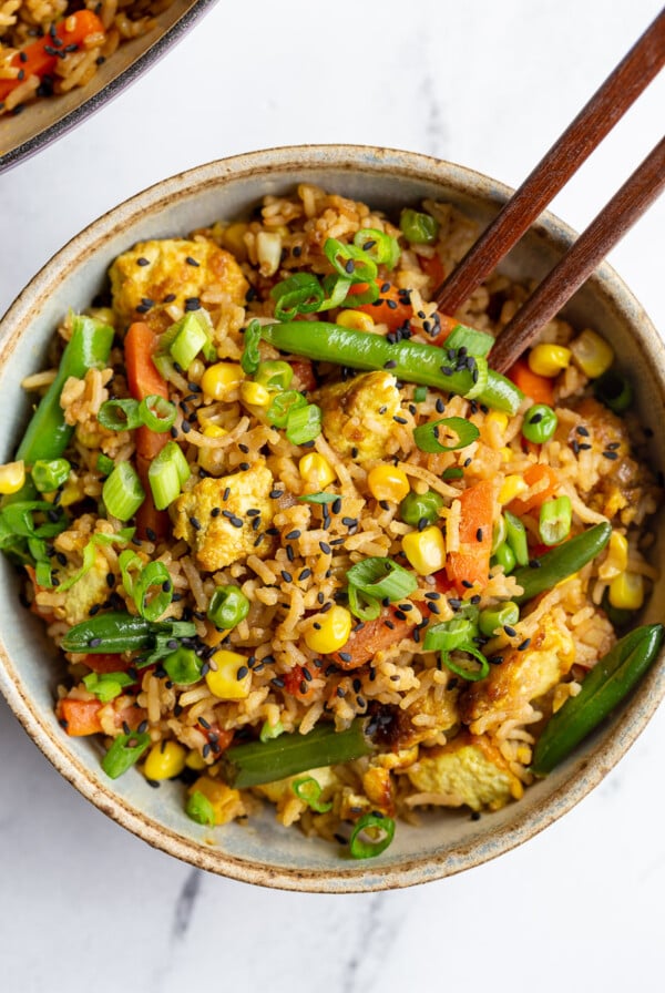 tofu fried rice with veggies in a small bowl with chopsticks sticking out the side