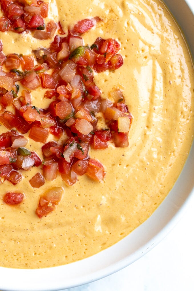 tofu queso cheese dip in a large bowl topped with pico de gallo