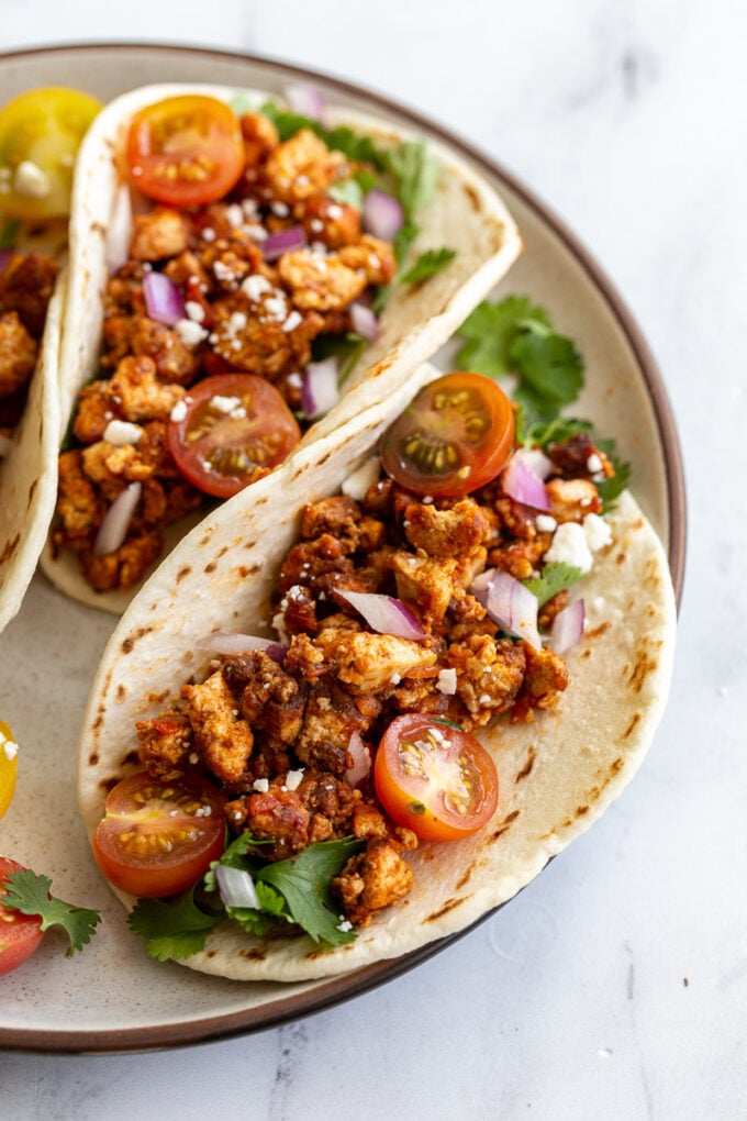 flour tortilla filled with tofu taco meat and topped with cherry tomatoes, cilantro, onion, and feta