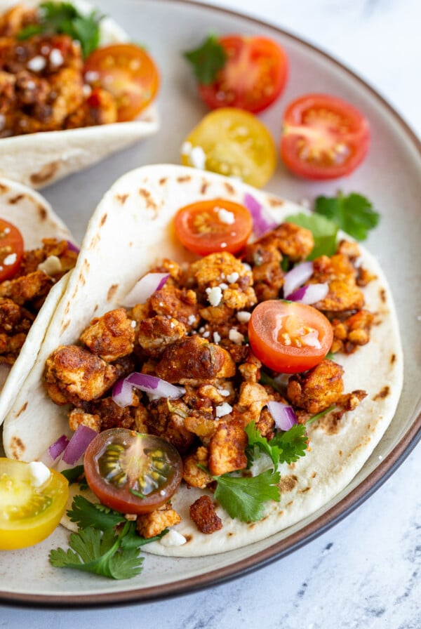 flour tortilla filled with tofu taco meat and topped with cherry tomatoes, cilantro, onion, and feta