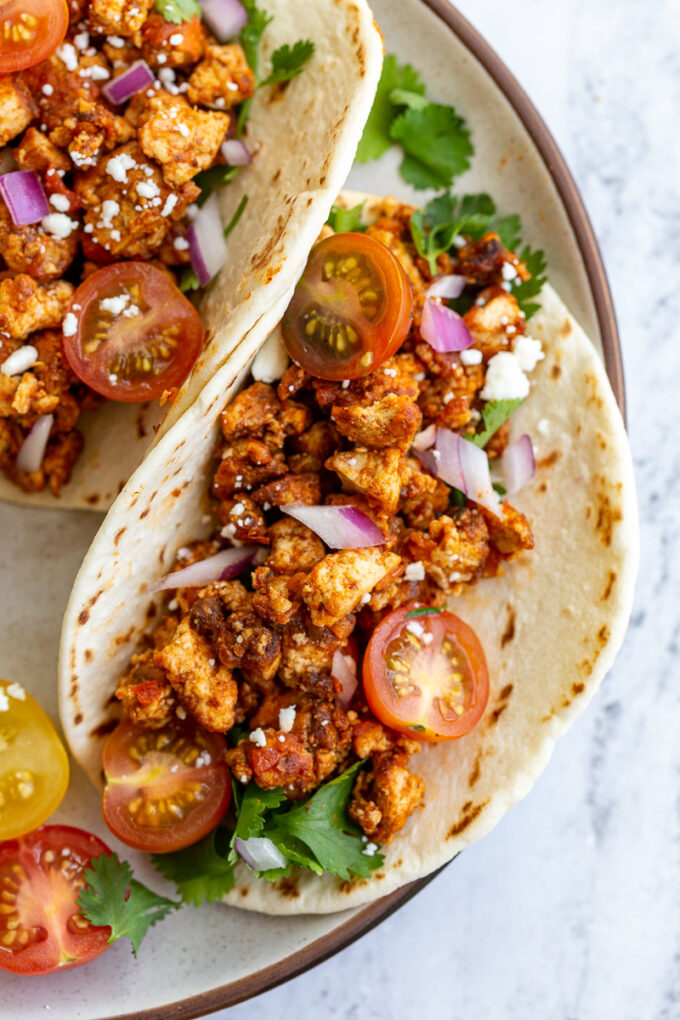 flour tortilla filled with tofu taco meat and topped with cherry tomatoes, cilantro, onion, and feta