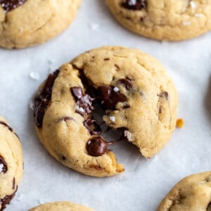 chocolate chunk cookies on a white background. the middle cookie is slightly cracked in half with melted chocolate coming out