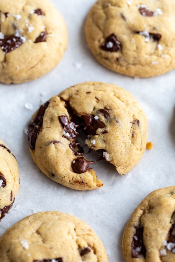 chocolate chunk cookies on a white background. the middle cookie is slightly cracked in half with melted chocolate coming out