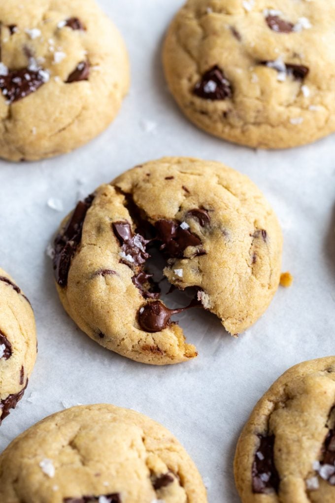 chocolate chunk cookies on a white background. the middle cookie is slightly cracked in half with melted chocolate coming out