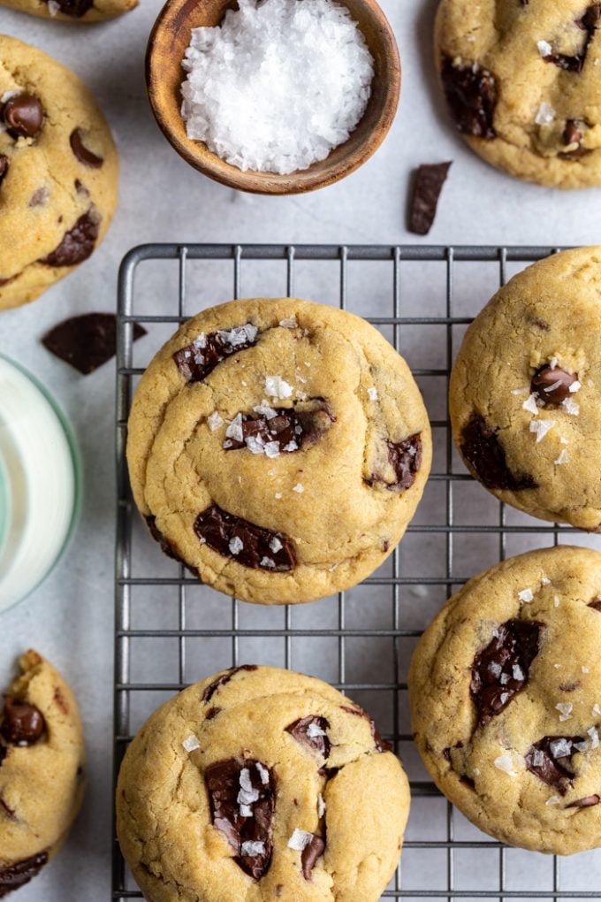 Vegan chocolate chip cookies of a cooling rack and topped with a bit of flaky sea salt