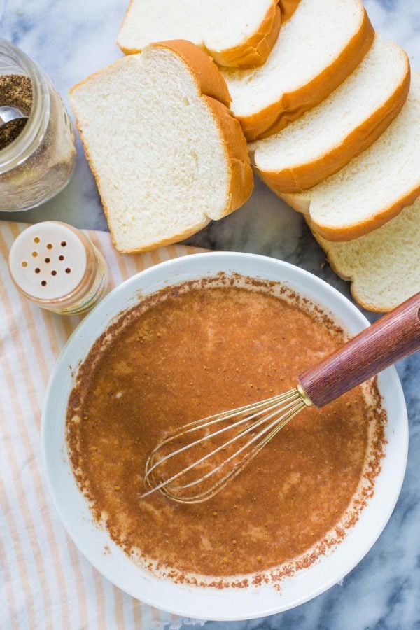 top down shot of ingredients for vegan french toast: bread, cinnamon, flaxseed meal, all whisked together in a shallow bowl