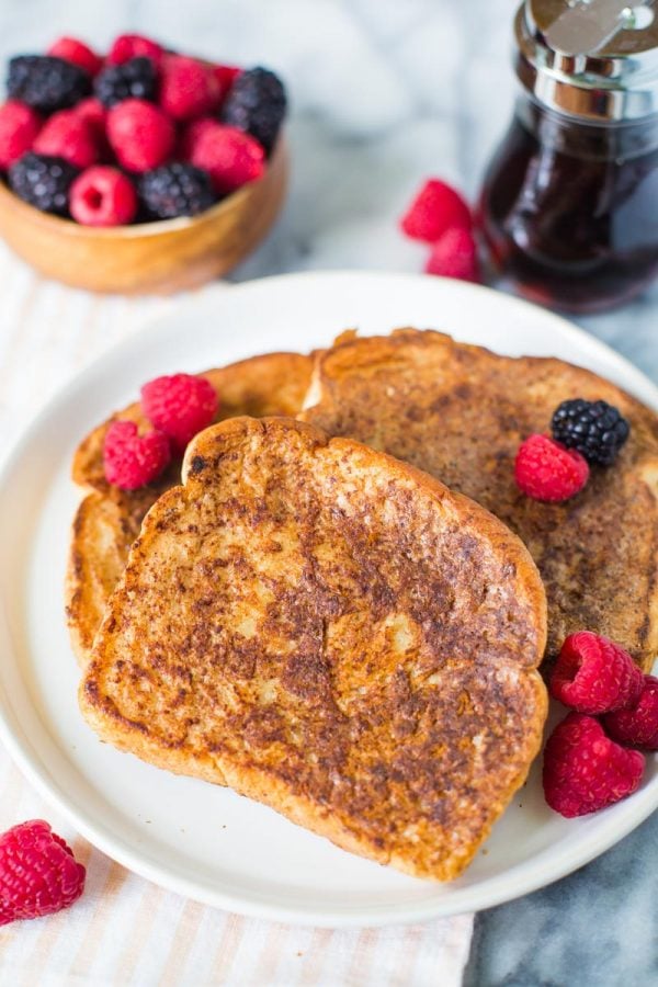 several slices of vegan french toast on a white plate topped with raspberries and blackberries