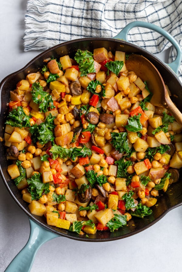 stirring vegan hash with a wooden spoon in a large skillet