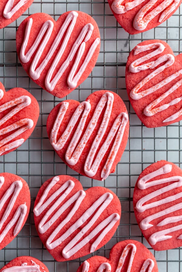 red heart cookies on a cooling rack topped with a light pink zig zag frosting