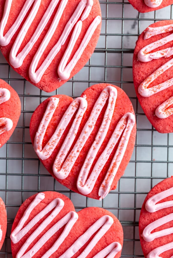 red heart cookies on a cooling rack topped with a light pink zig zag frosting