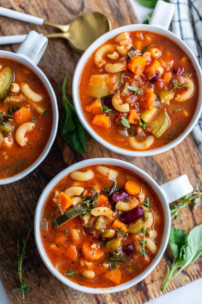 vegan minestrone soup in soup cups. the cups are sitting on a wood board